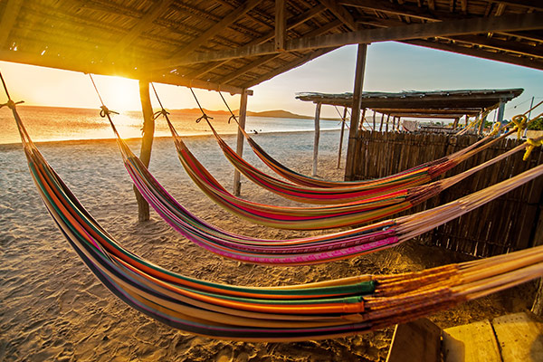 Cinco hamacas coloridas colgadas debajo de una casa de guadua en la playa de Santa Marta, forman parte del plan turístico para viajar por la costa caribe colombiana