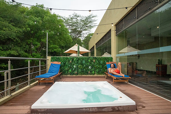 Jacuzzi exterior frente a dos sillas playeras, una de ellas ocupada por un hombre quien se encuentra recostado con una pantaloneta roja, apreciando el paisaje del Hotel Waya Albania y disfrutando uno de los planes vacacionales todo incluido en La Guajira