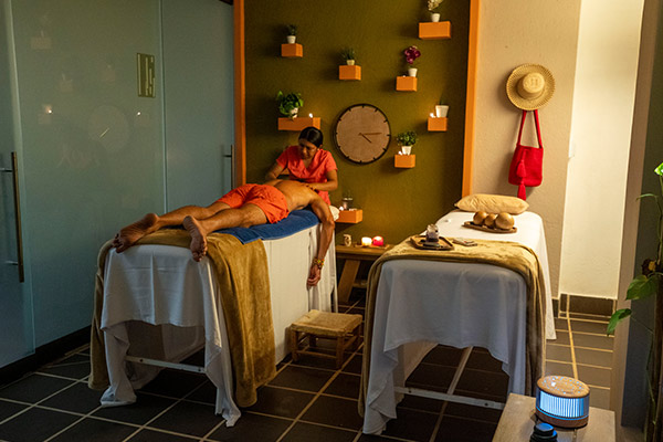 Salón de spa, con dos camillas, una de ellas ocupada por un hombre a quien le realizan masajes. Servicios como estos se encuentran en los planes vacacionales todo incluido en La Guajira